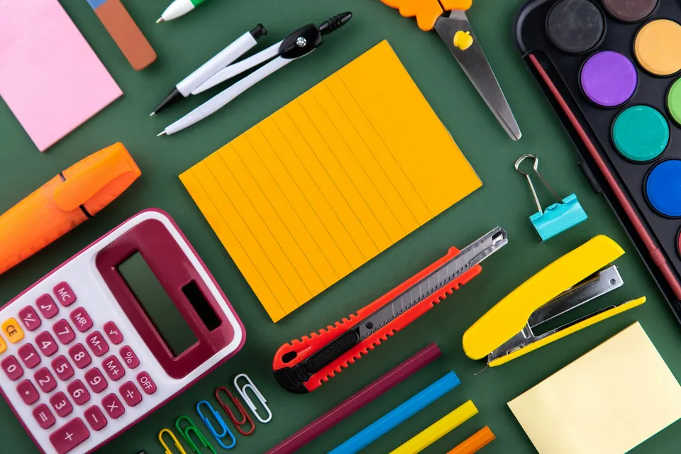 A calculator, sticky notes, scissors and a stapler laid out on a desk