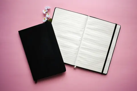 A black notebook and an open ruled notebook on a desk