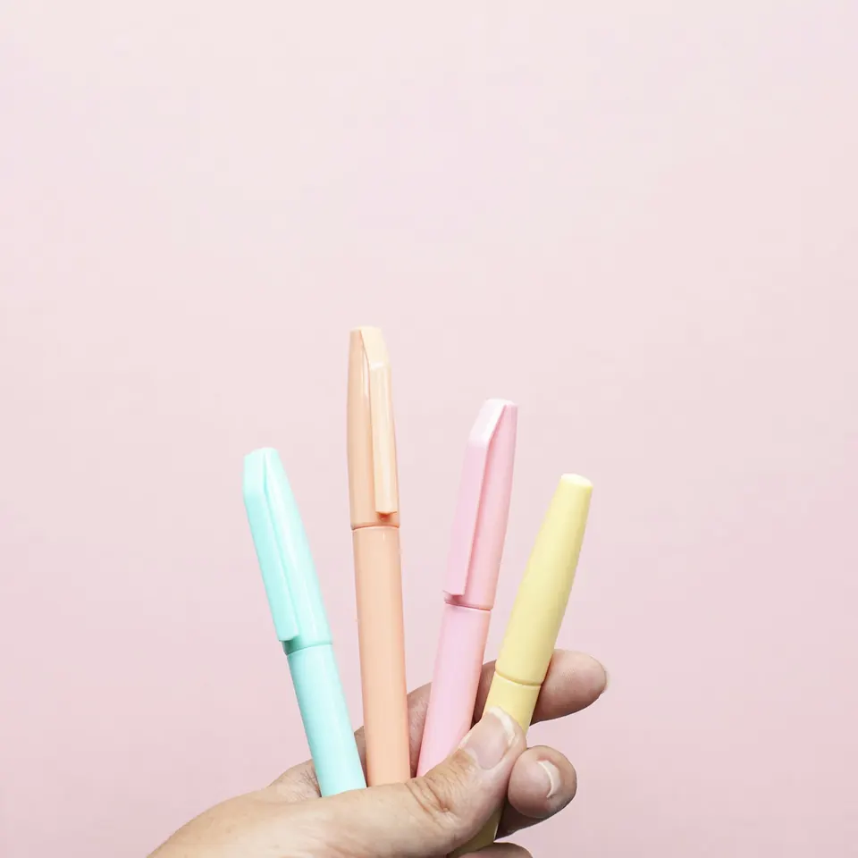 Four pastel highlighters held against a pink wall
