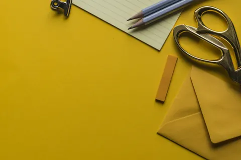 Scissors, pencils and an envelope on a yellow desk