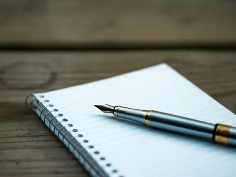 A spiral-bound ruled notebook with a fountain pen on top